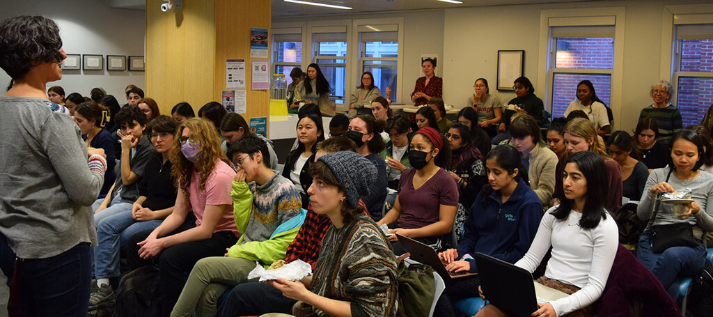 People seated and standing listening to a speaker.